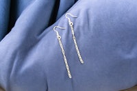 a pair of silver earrings on a blue cloth